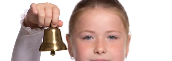 Young school girl ringing a golden bell on white background focu