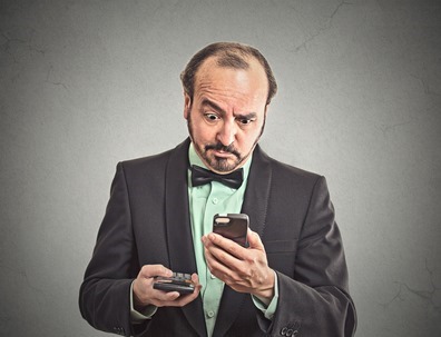 surprised businessman looking on smart phone holding calculator 